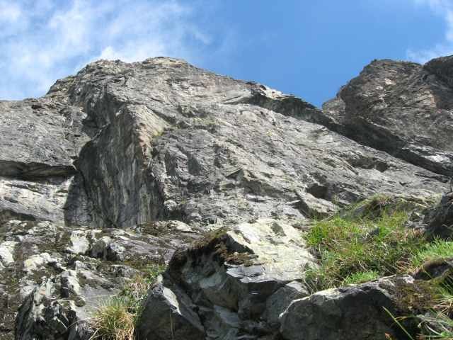 La voie part dans le rocher moussu et ensuite dans la face, à droite des dalles blanches et noires