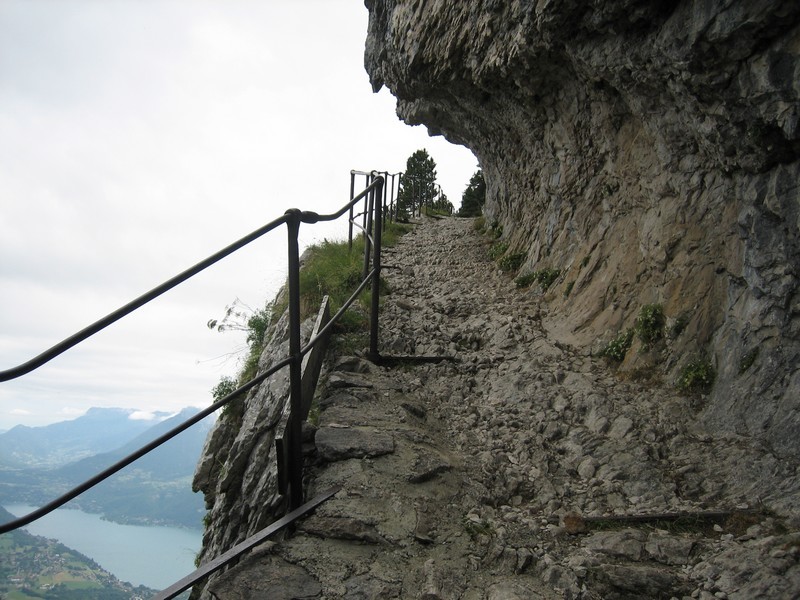 Chemin taillé dans la falaise sur fond de lac d'Annecy